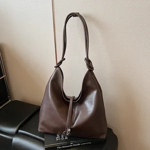 Brown leather hobo tote bag with knot detail and metallic ring charm on a dark base