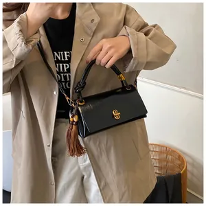 Detail view of black faux leather underarm bag with gold twist lock and brown tassels