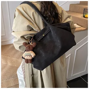Détail d'un sac cabas noir mat avec pendentif ours en peluche et longue bandoulière réglable