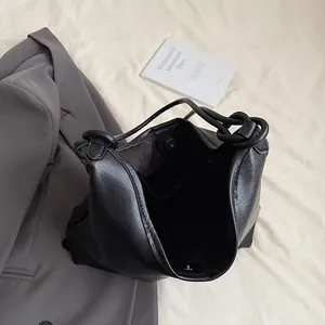 Minimalist black leather tote bag with unique knotted shoulder straps and magnetic buckle