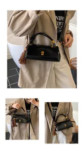 Detail view of black faux leather underarm bag featuring gold clasp and brown tassel accent