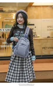 Grayish purple nylon crossbody bag with metal zippers and round logo in an urban cafe setting