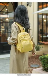 Outdoor shot of a bright yellow compact backpack featuring a front pocket and side slots
