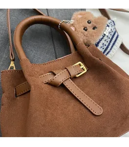 Close-up of brown suede handbag with golden hardware and a cute puppy plush charm