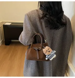 Detail showing high-capacity pleated dark brown suede handbag with a plush dog charm