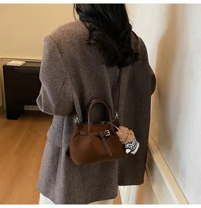 Detail of dark brown suede handbag with leather buckle and plush bear charm accent