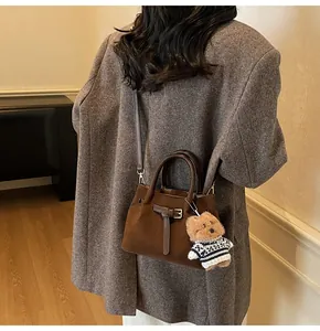 Detail of dark brown matte leather handbag with vintage buckle and plush bear pendant accessory