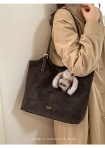 Dettaglio borsa tote in pelle scamosciata marrone scuro con logo e ciondolo a coniglio