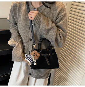 Detail of black suede tote bag featuring a cute teddy bear charm and metal buckle strap