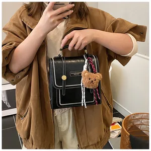 Detail of black leather backpack with white stitching, gold buckle and brown bear charm