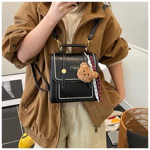 Close-up of black leather mini backpack with gold buckle, plush bear and ribbon charm