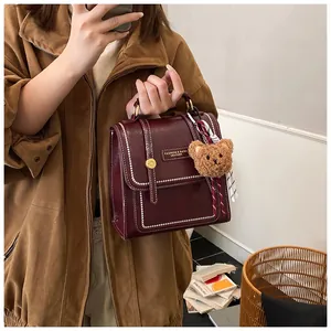 Close-up of burgundy leather handbag with bear pendant and decorative silk scarf detail