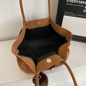 Brown suede tote bag with magnetic closure and plush ball charm in a minimalist style