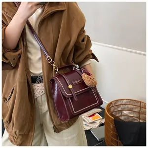 Close-up of vintage deep red leather handbag with white stitching and bear charm