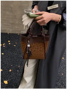 Détail du sac seau à imprimé léopard avec bordure en cuir marron et breloques en métal