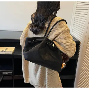 Close-up of black suede tote bag with decorative wooden beads and tassel on long shoulder straps