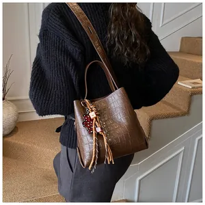 Detail of dark brown croc-embossed bucket bag with red bear charm and woven strap accessory