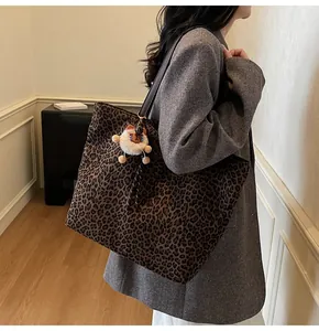 Detail view of large leopard print tote bag with brown leather strap and plush bear charm