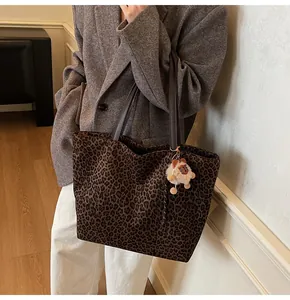 Detail of leopard print tote bag with brown leather handles and plush bear charm