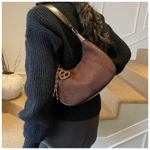 Borsa a mezzaluna in camoscio marrone portata a spalla in un ambiente vintage sobrio