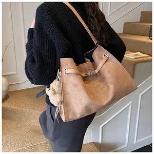 Macro detail of brown suede tote bag with silver buckle and plush bear pendant accessory