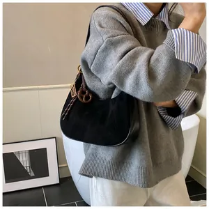 Dettaglio della borsa sottobraccio nera con ciondolo dorato su un maglione grigio