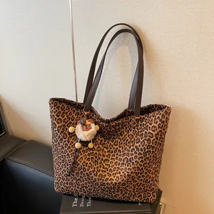 Chic leopard print tote bag with brown straps and plush bear charm on a sofa