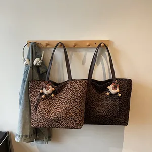 Large leopard print tote bags with bear charm hanging on a rack with denim jacket