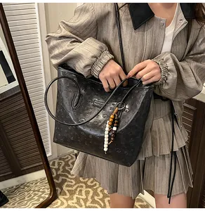 Close-up of black embossed tote bag with wood bead charm on a striped jacket model