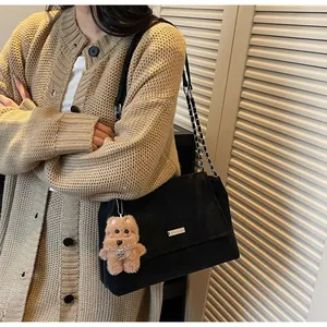 Detalle de bolso de hombro en ante negro con cadena plateada y un colgante de perro de peluche