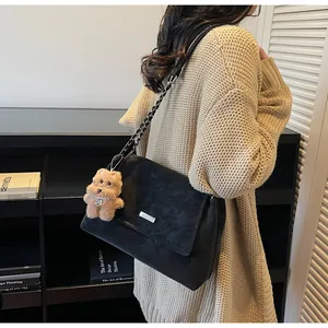 Detalle de bolso de ante negro con cadena plateada y colgante de osito de peluche marrón
