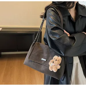 Detalle de bolso de hombro de ante marrón oscuro con cadena y colgante de perro