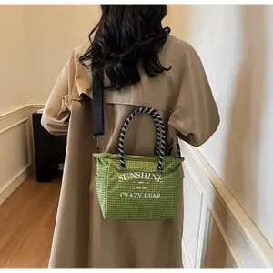 Detail of green plaid canvas tote bag with white typography and removable shoulder strap