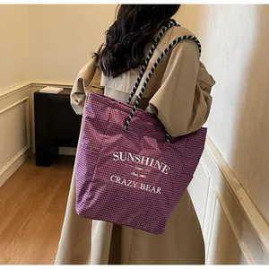 Detail of purple plaid tote bag with rope handles and white lettering in a lifestyle setting