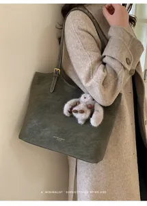 Detail of dark green vintage tote bag with plush rabbit charm on beige wool coat