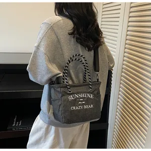 Detail of checkered tote bag with rope handles and logo print shown by a model