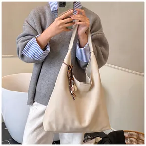 Detail of cream leather shoulder bag with wide strap and brown woven tassel charm