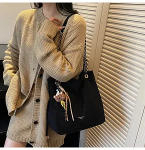Detail of black leather tote bag with chain strap and cute bear charm worn by a model