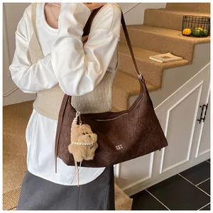 Detail of dark brown pleated leather tote bag with metallic logo and plush bear charm