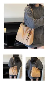 Macro view of khaki suede tote bag with chain strap and cartoon bear charm detail