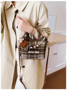 Detail einer braunen Karo-Handtasche aus Wolle mit Plüschbär-Anhänger und Perlen