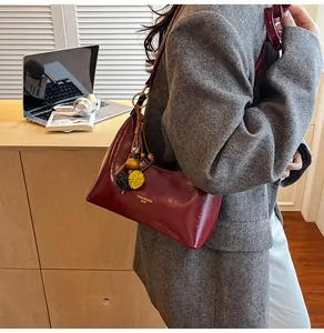 Detail of burgundy glossy oil-waxed leather crescent bag with decorative floral charm