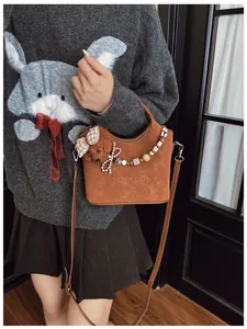 Detail der braunen matten Beuteltasche mit süßem Bärenanhänger und bunter Perlenkette