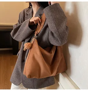 Detail of caramel brown suede hobo bag featuring wide strap and woven knot pendant