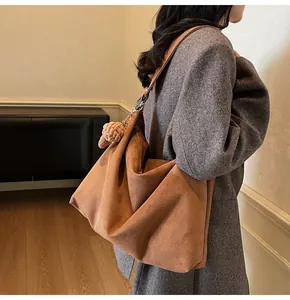 Detail of a large brown slouchy suede tote bag with decorative pompom on a model