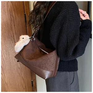 Detalle de bolso tote marrón vintage con textura plisada y colgante de pato