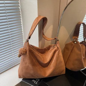 Large caramel suede tote bag with pompom charm shown in a warm natural light setting