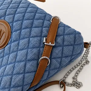 Detail of blue denim tote bag with quilted stitching, brown leather trim and silver metal buckle