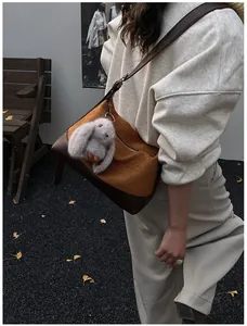 Detalle del bolso tote de tela naranja texturizada con correa de cuero marrón y conejo de peluche