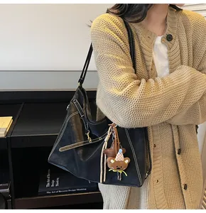 Detail of black leather tote bag with white stitching and bear charm on beige cardigan